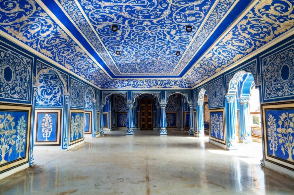A hallway inside the City Palace Jaipur, Rajasthan, adorned with exquisite wall art paintings and intricate floral patterns.