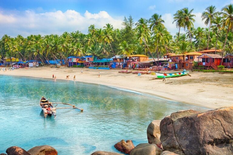 Scenic view of Palolem Beach in Goa, India, as featured in the Goa Travel Guide, with fishing boats on the shoreline and serene waters with scattered stones.