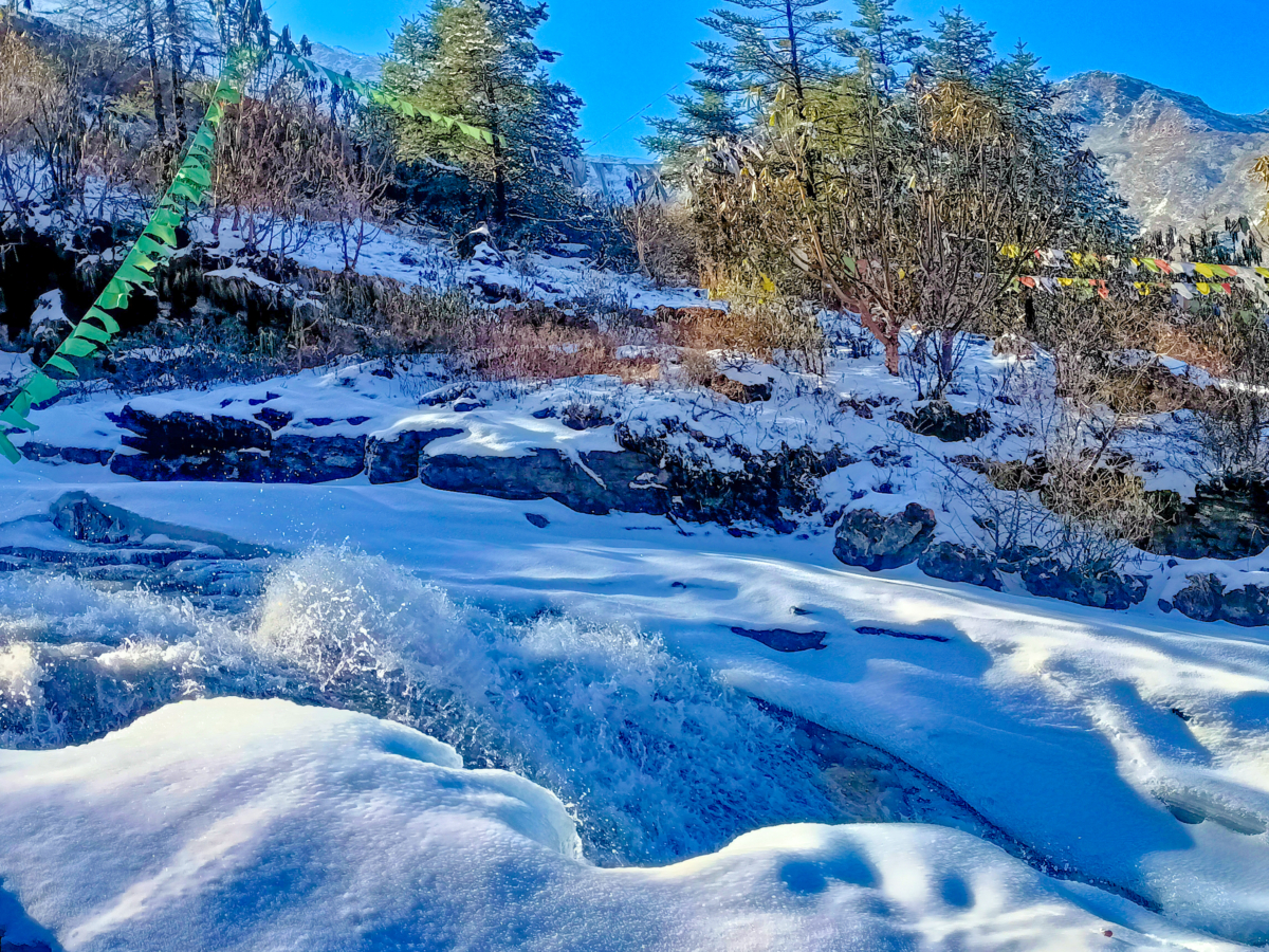 Early winter's frozen stream near Mount Katao, in North Sikkim showcasing a brown rugged terrain adorned with interspersed white snow accumulation.
