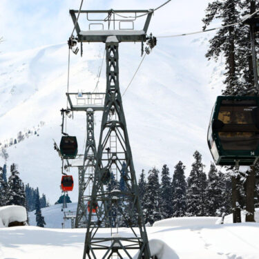 Skiers and tourists ride in a gondola lift, passing over the snow-covered slopes of the famous Gulmarg ski resort in Baramulla district, Jammu and Kashmir, India, on February 12, 2023. The gondola lift offers views of the Himalayan mountains and provides access to higher reaches for winter sports enthusiasts. (Photo by Nasir Kachroo/NurPhoto via Getty Images)