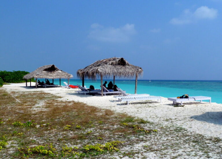 A serene view of Kadmat Beach, a Blue Flag-certified paradise, featuring pristine white sands, crystal-clear turquoise waters, and well-arranged beach setups with sun loungers and umbrellas for a perfect tropical retreat.