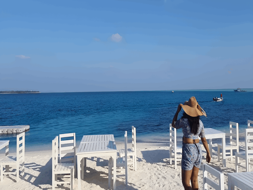 6 Nights 7 Days Agatti-Kavaratti-Bangaram-Thinnakara Affordable Luxury Lakshadweep Package by SetMyTrip – White sandy beach with oceanfront dining setup and tourist enjoying the sea view.