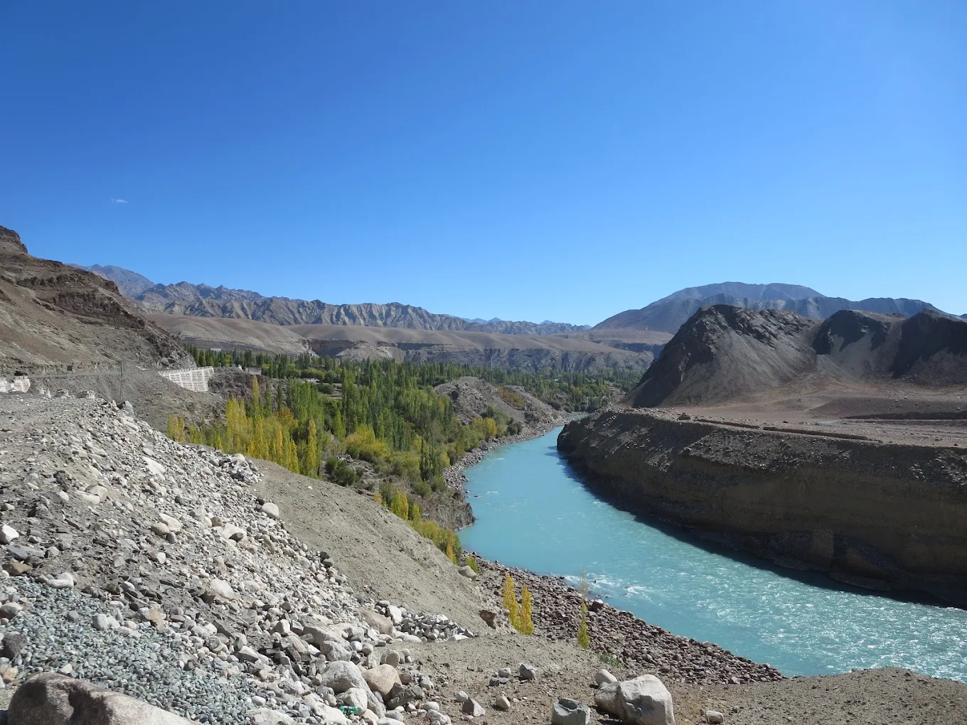 The Indus River flowing through Phobe La, a quiet mountain pass between Likir and Saspol, showcasing Ladakh’s contrasting beauty of desert hills and green riverbanks under a crystal-clear sky.