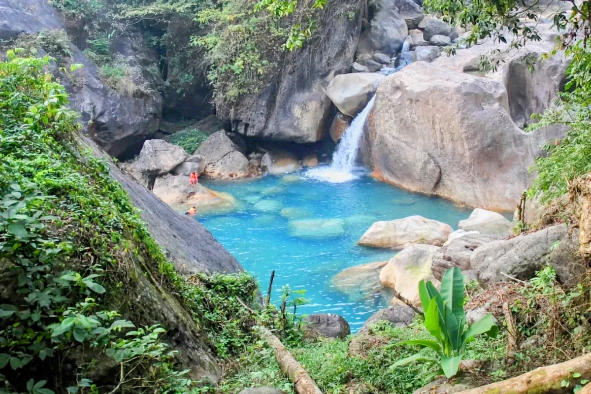 Blue Lagoon in Meghalaya with turquoise waters and green cliffs, featured in adventure packages with trekking, caving, kayaking, and living root bridge trails.