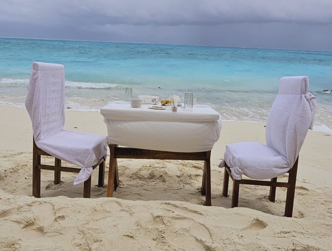 SetMyTrip 4 Nights Lakshadweep Agatti Honeymoon Package – includes a private beach celebration set-up with an intimate dining table arranged on the white sands of Agatti Island, offering couples a romantic daytime experience by the turquoise sea.