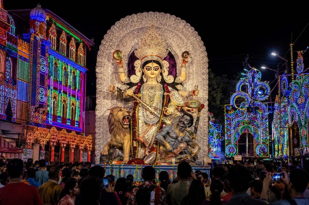 Jagaddhatri idol during the Chandannagar Puja immersion procession, surrounded by colourful festival lights and crowds at night.