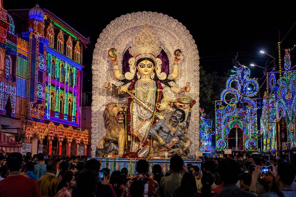 Jagaddhatri idol during the Chandannagar Puja immersion procession, surrounded by colourful festival lights and crowds at night.